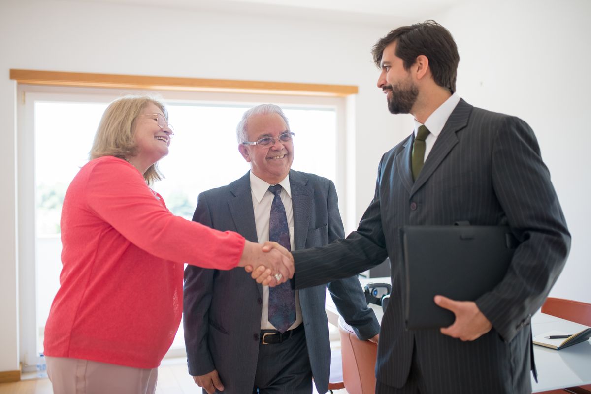 A happy senior couple sharing a Red Deer REALTOR review moment, shaking hands with Carrie Meir after a successful home sale.A happy senior couple shaking hands with their REALTOR® after a successful home sale in Central Alberta.