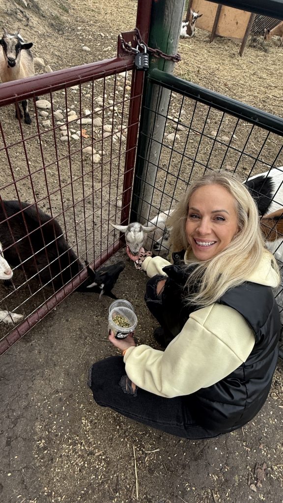 Carrie Meir crouched by the goat pen feeding goats at Kraay Family Farm in Lacombe