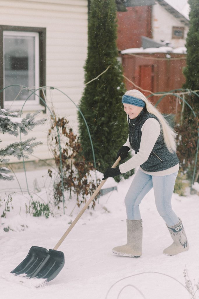 Woman shovelling snow from the walkway outside her house in winter